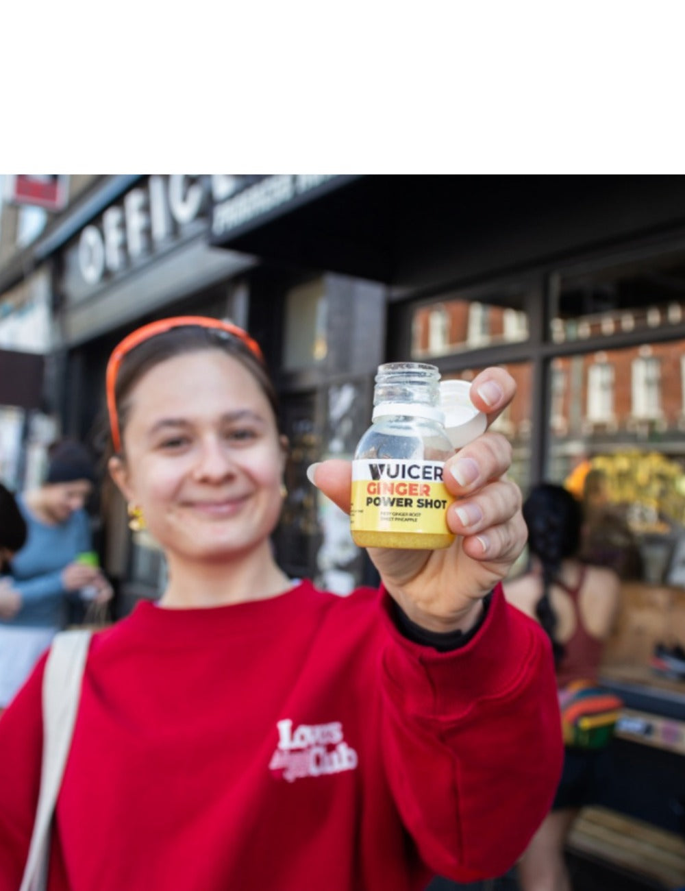 woman smiling holding a vuicer ginger shot